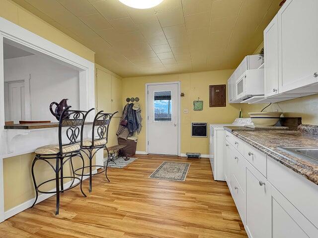 kitchen with white cabinetry, sink, electric panel, and light hardwood / wood-style floors