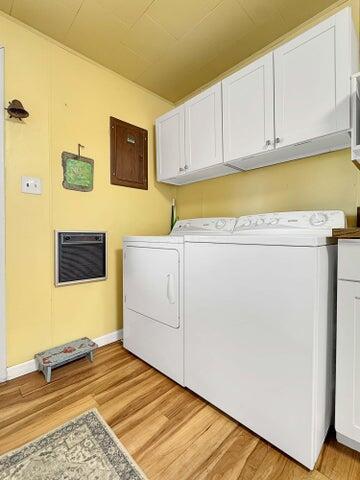 washroom featuring heating unit, cabinets, light wood-type flooring, electric panel, and washing machine and dryer