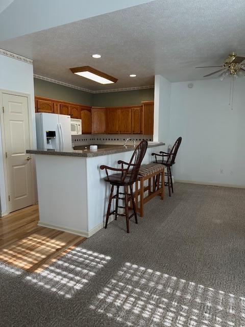 kitchen with light carpet, a textured ceiling, a kitchen breakfast bar, kitchen peninsula, and white appliances