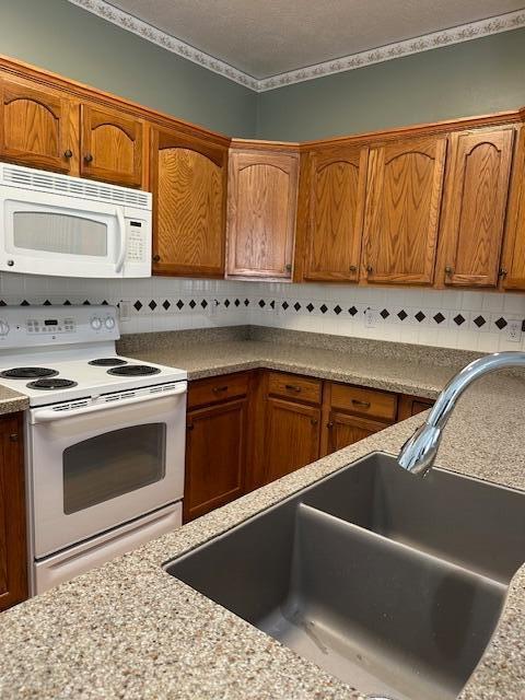 kitchen featuring tasteful backsplash, white appliances, sink, and a textured ceiling