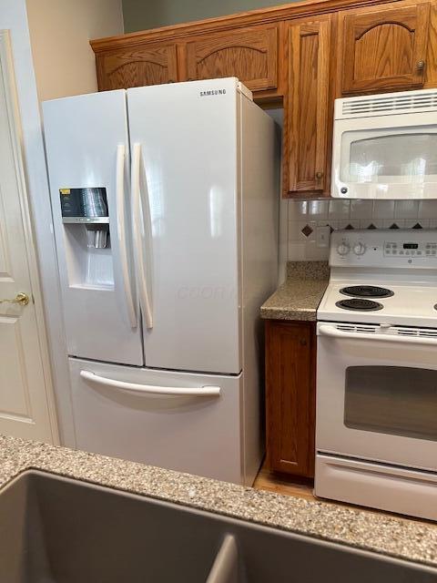 kitchen featuring white appliances, light stone countertops, and backsplash