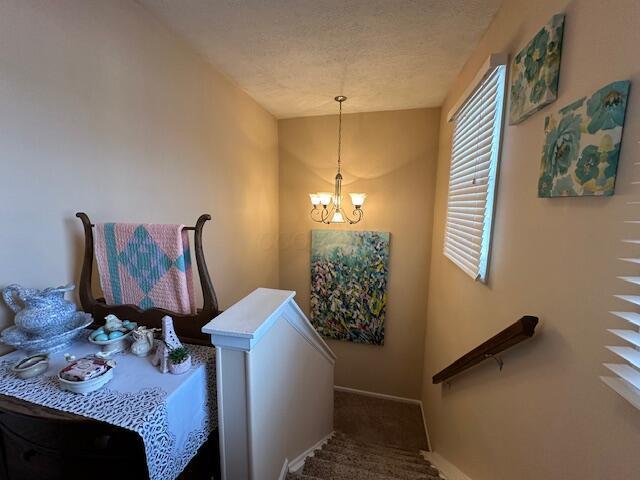 stairs with an inviting chandelier, carpet, and a textured ceiling