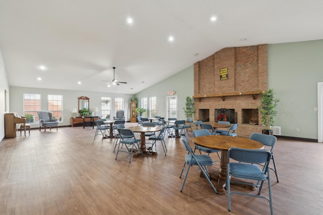 dining space with a wealth of natural light, a fireplace, high vaulted ceiling, and light wood-type flooring