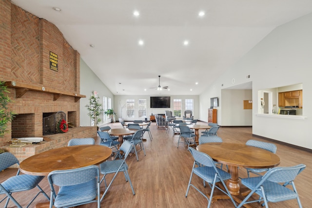 dining room with ceiling fan, a brick fireplace, high vaulted ceiling, and light hardwood / wood-style floors