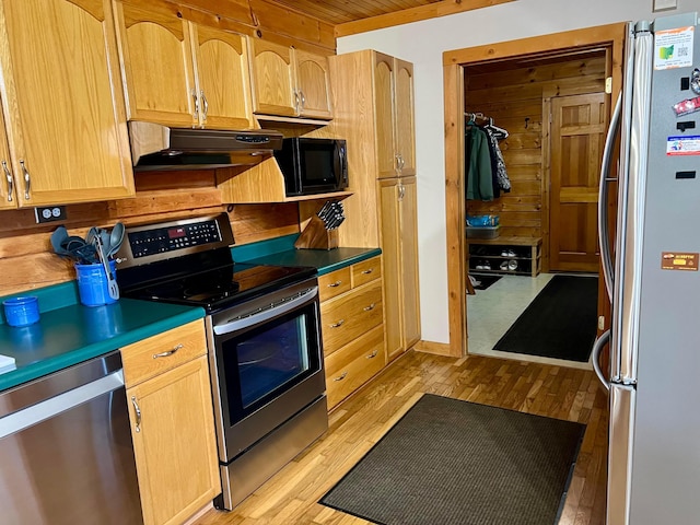 kitchen with stainless steel appliances, light hardwood / wood-style floors, and wood walls