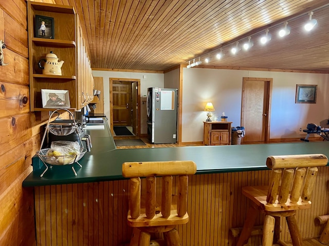 kitchen featuring sink, wood ceiling, stainless steel fridge, and a kitchen breakfast bar