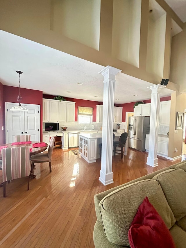 living room featuring light wood-type flooring, a high ceiling, and ornate columns