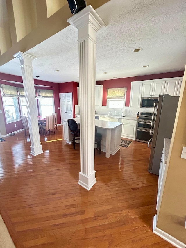 kitchen featuring white cabinetry, decorative columns, stainless steel appliances, wood-type flooring, and a kitchen island