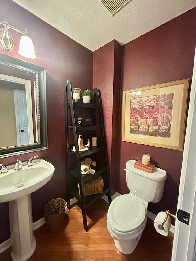 bathroom featuring wood-type flooring, toilet, sink, and a textured ceiling