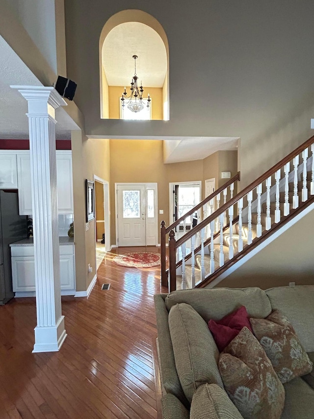 foyer entrance with a towering ceiling, wood-type flooring, a chandelier, and ornate columns