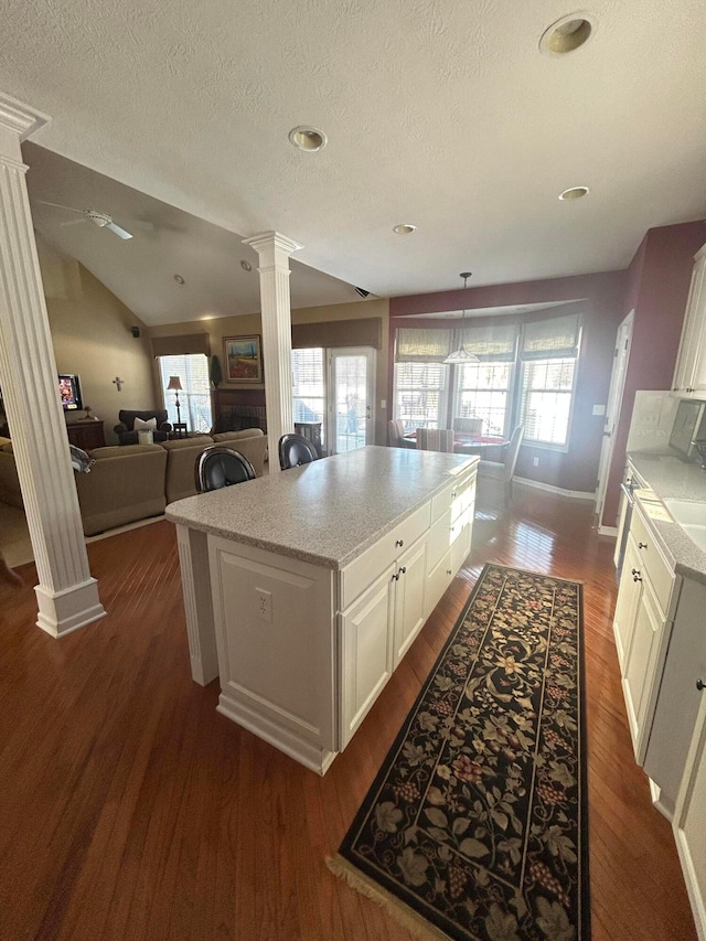 kitchen with white cabinetry, decorative columns, dark hardwood / wood-style floors, a center island, and vaulted ceiling