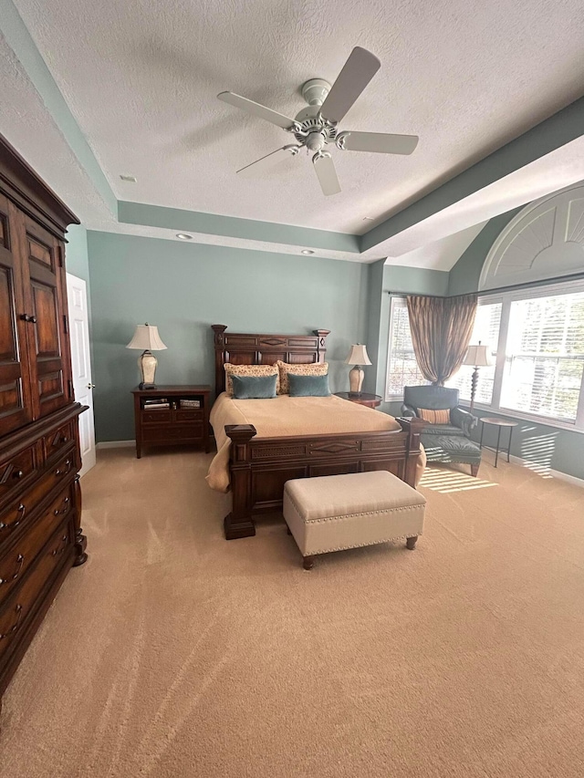 carpeted bedroom with ceiling fan, a tray ceiling, and a textured ceiling