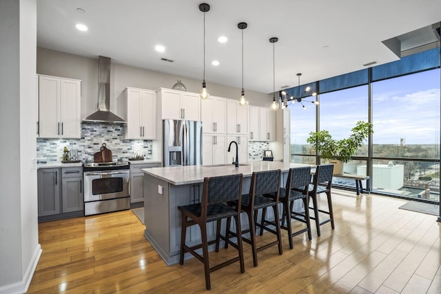 kitchen featuring gray cabinets, pendant lighting, white cabinetry, stainless steel appliances, and wall chimney exhaust hood