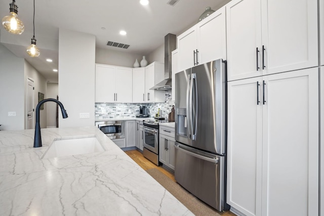 kitchen with sink, white cabinets, light stone counters, stainless steel appliances, and wall chimney range hood