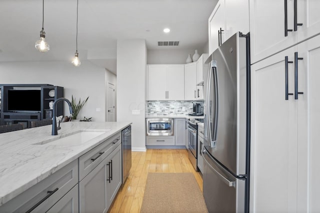 kitchen featuring sink, decorative light fixtures, light hardwood / wood-style flooring, stainless steel appliances, and white cabinets