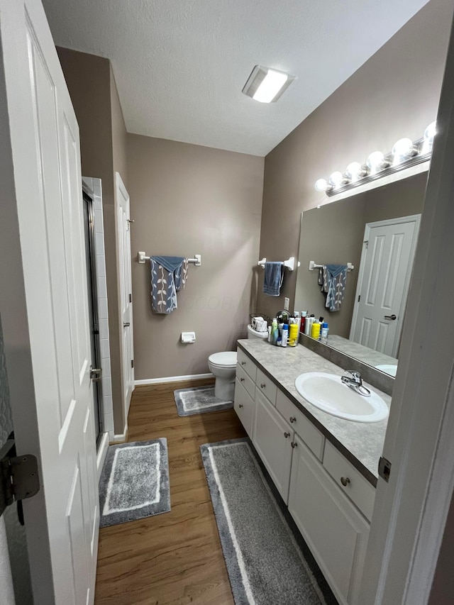 bathroom with walk in shower, toilet, a textured ceiling, vanity, and hardwood / wood-style floors