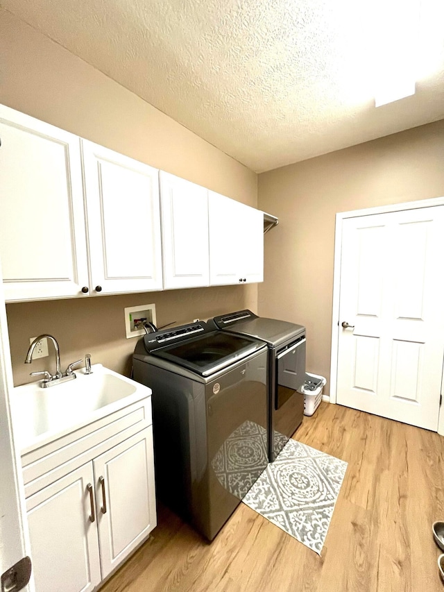 laundry room featuring sink, cabinets, light hardwood / wood-style floors, a textured ceiling, and washing machine and clothes dryer