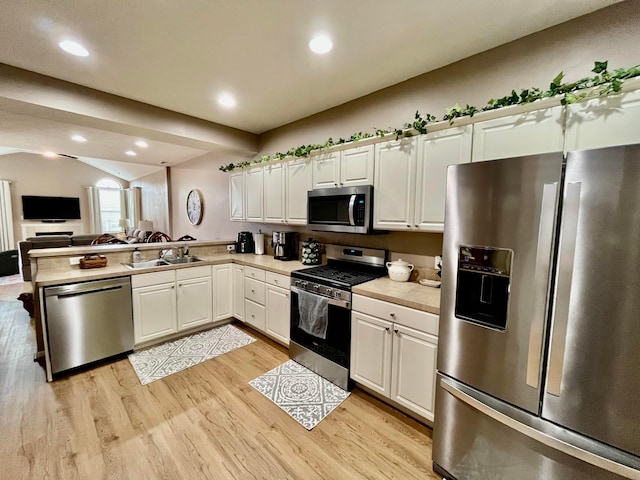 kitchen with vaulted ceiling, appliances with stainless steel finishes, white cabinetry, sink, and kitchen peninsula