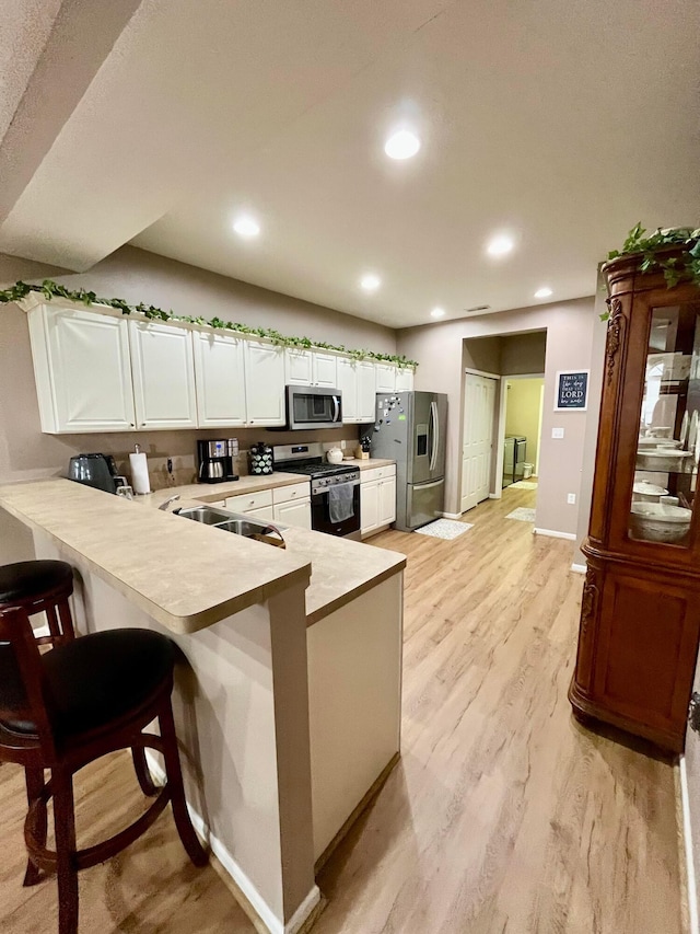 kitchen with a breakfast bar area, white cabinets, kitchen peninsula, stainless steel appliances, and light hardwood / wood-style flooring