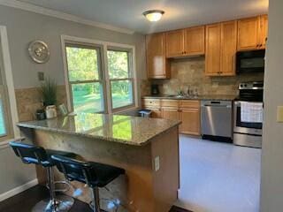 kitchen featuring a breakfast bar area, appliances with stainless steel finishes, backsplash, ornamental molding, and kitchen peninsula