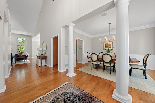 foyer entrance featuring an inviting chandelier, a towering ceiling, light hardwood / wood-style flooring, and decorative columns