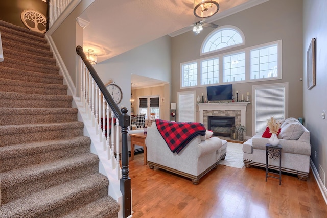 living room with hardwood / wood-style flooring, crown molding, a stone fireplace, and a towering ceiling