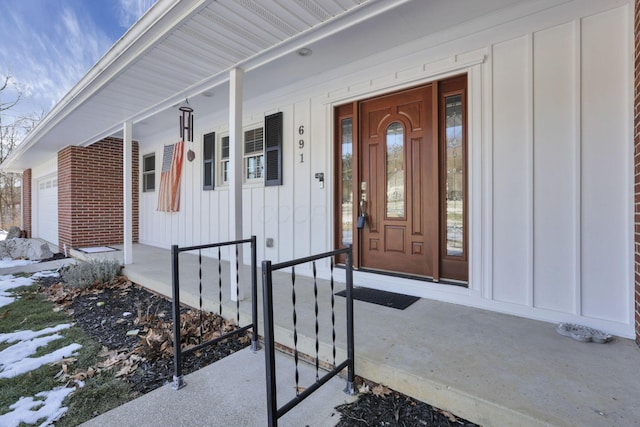 snow covered property entrance with a garage and covered porch