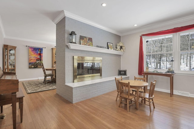 dining space with crown molding, a fireplace, and light wood-type flooring