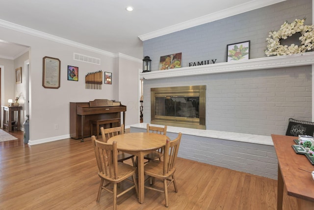 dining room featuring ornamental molding, a fireplace, light hardwood / wood-style floors, and brick wall