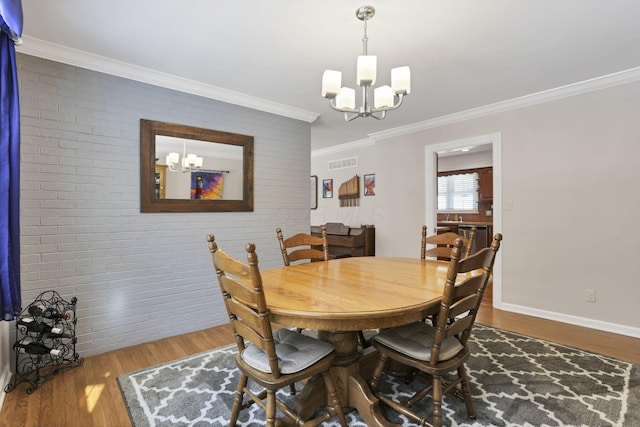 dining room featuring hardwood / wood-style flooring, crown molding, brick wall, and an inviting chandelier