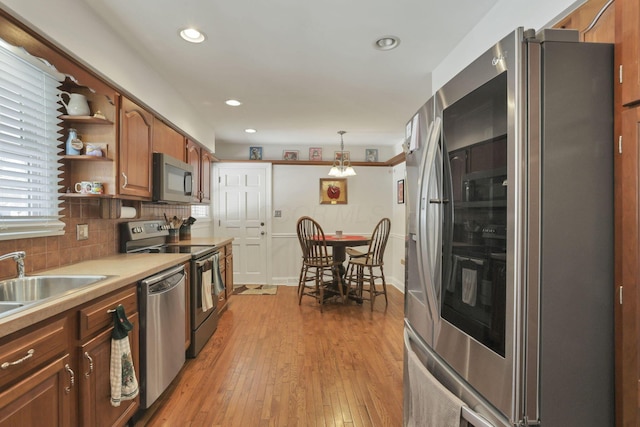 kitchen featuring sink, stainless steel appliances, tasteful backsplash, light hardwood / wood-style floors, and decorative light fixtures