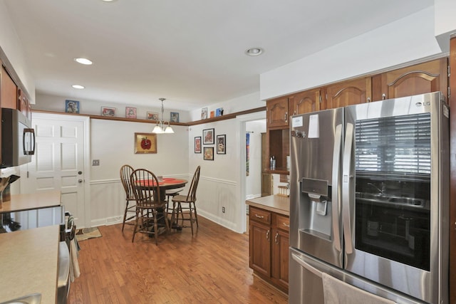 kitchen with hanging light fixtures, appliances with stainless steel finishes, and light hardwood / wood-style floors