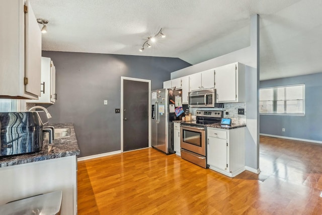 kitchen with vaulted ceiling, stainless steel appliances, dark stone counters, and white cabinets