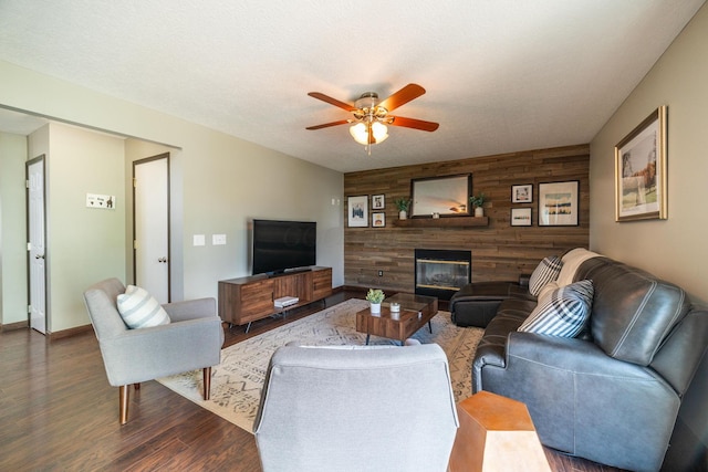 living room with a textured ceiling, dark wood-type flooring, ceiling fan, and wood walls