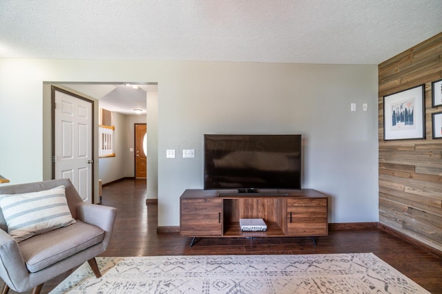 living room with dark wood-type flooring, wooden walls, and a textured ceiling