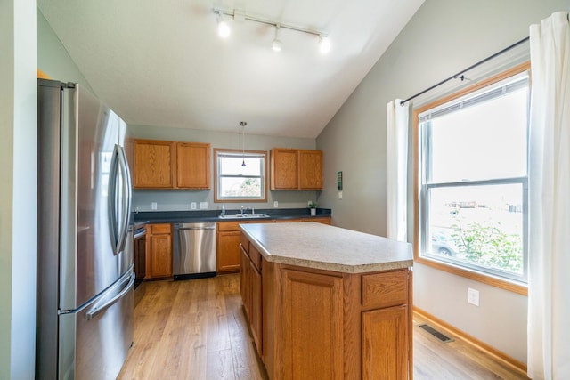 kitchen with stainless steel appliances, decorative light fixtures, a kitchen island, and light wood-type flooring