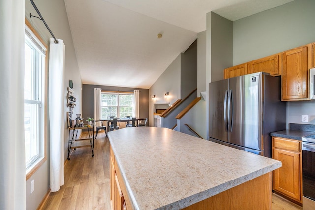 kitchen featuring stainless steel appliances, vaulted ceiling, a center island, and light hardwood / wood-style flooring