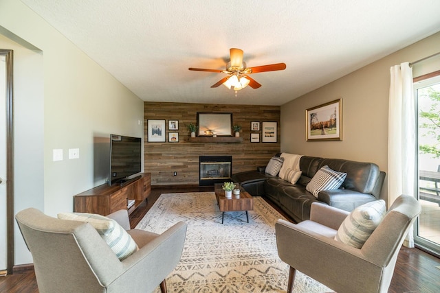 living room with dark hardwood / wood-style flooring, ceiling fan, a textured ceiling, and wood walls