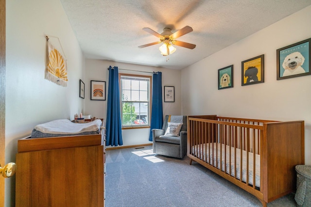 carpeted bedroom with ceiling fan, a textured ceiling, and a crib