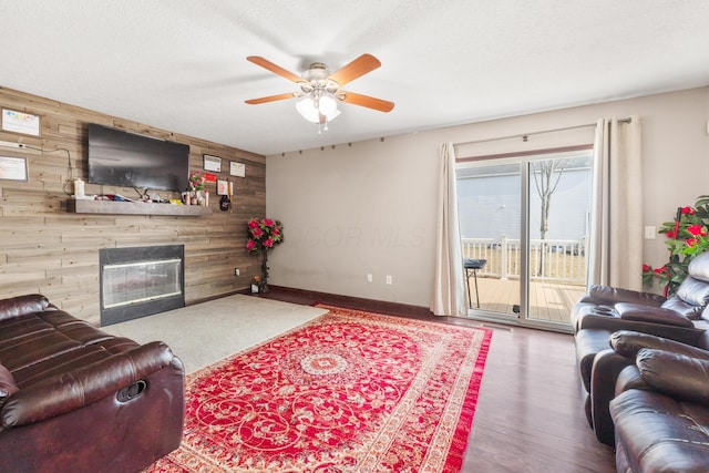 living room featuring hardwood / wood-style floors, wood walls, a large fireplace, ceiling fan, and a textured ceiling