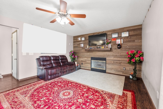 living room featuring ceiling fan, dark wood-type flooring, a fireplace, and wooden walls