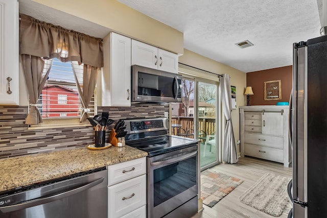 kitchen featuring visible vents, light wood-style floors, white cabinets, appliances with stainless steel finishes, and decorative backsplash