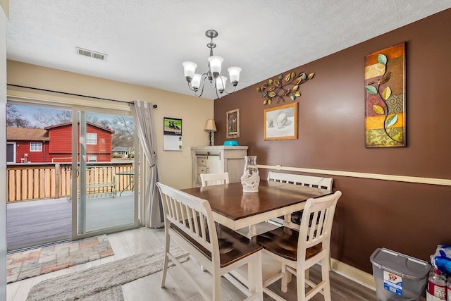 dining space with visible vents, a textured ceiling, wood finished floors, a chandelier, and baseboards