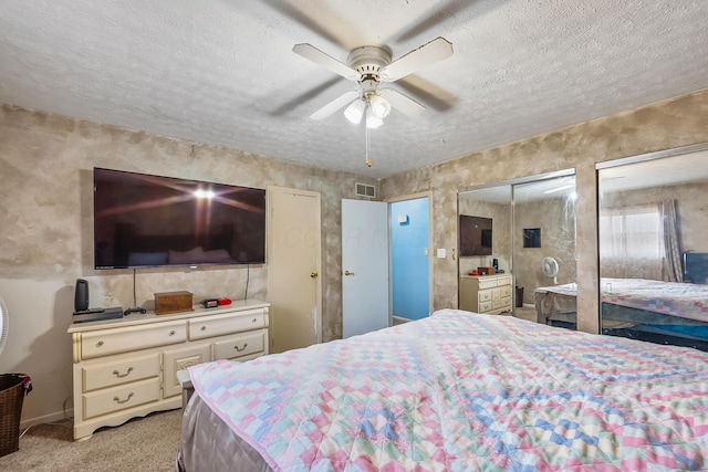 bedroom featuring visible vents, a ceiling fan, light colored carpet, a textured ceiling, and multiple closets