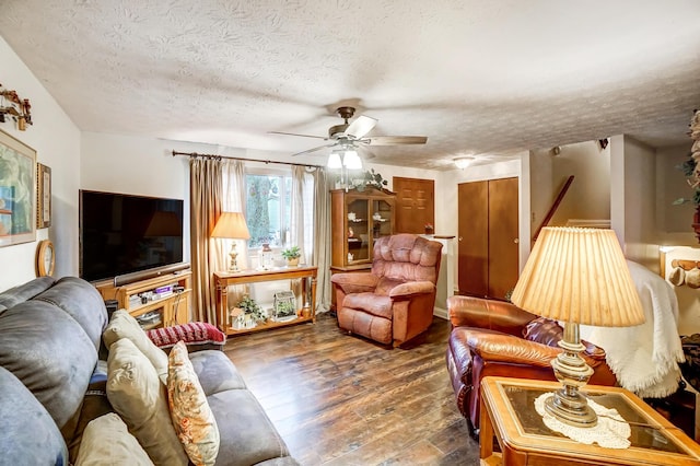 living room featuring dark wood-type flooring, ceiling fan, and a textured ceiling