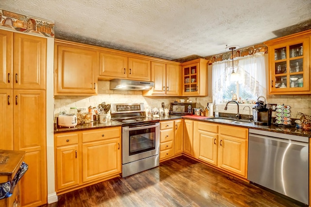 kitchen with appliances with stainless steel finishes, pendant lighting, sink, backsplash, and dark hardwood / wood-style flooring