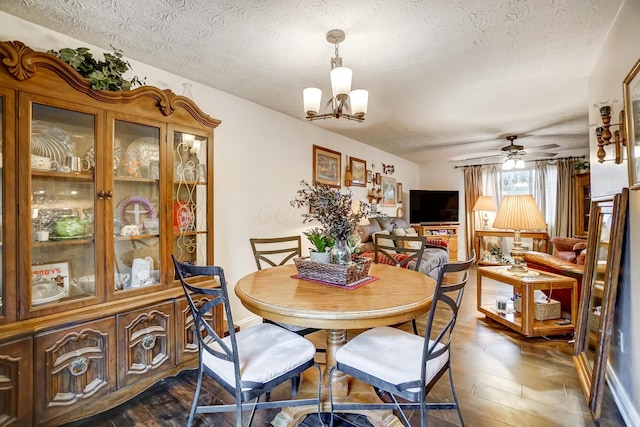 dining space with dark hardwood / wood-style floors, ceiling fan with notable chandelier, and a textured ceiling