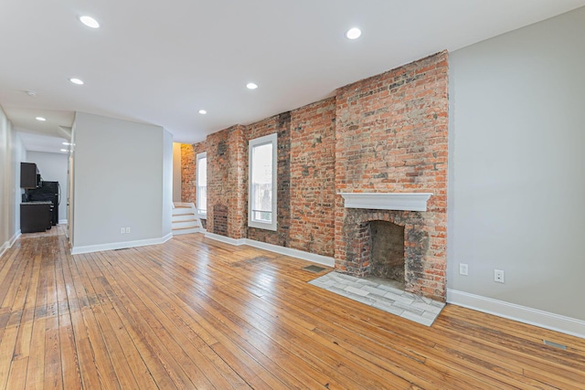 unfurnished living room with brick wall, a brick fireplace, and light wood-type flooring