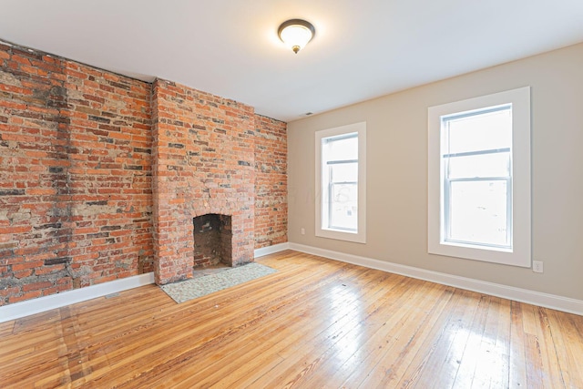 unfurnished living room featuring brick wall and light wood-type flooring