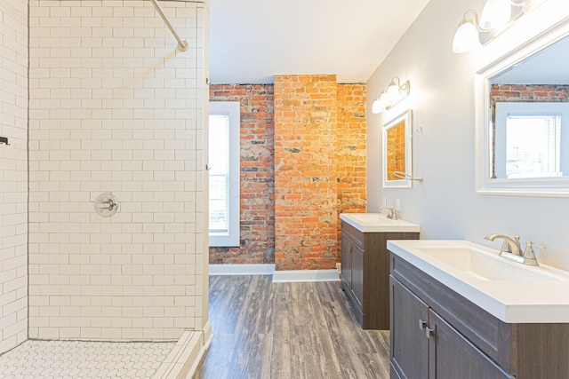 bathroom featuring brick wall, wood-type flooring, vanity, and a tile shower